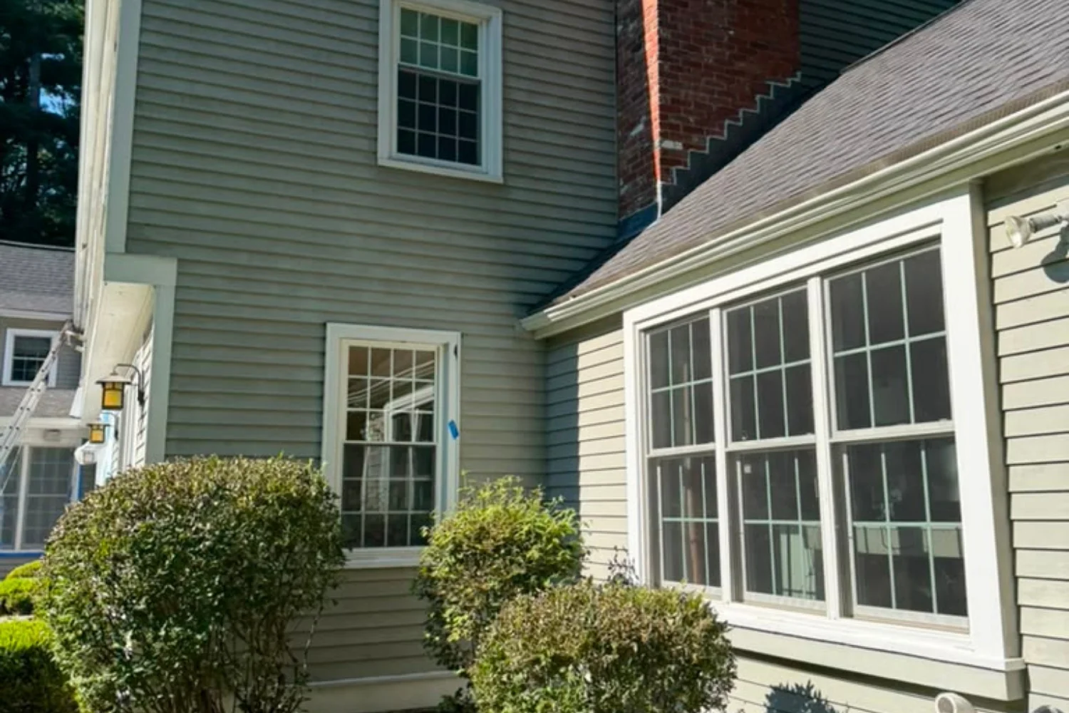 Detail of home exterior with sage siding, white-trimmed windows and brick chimney