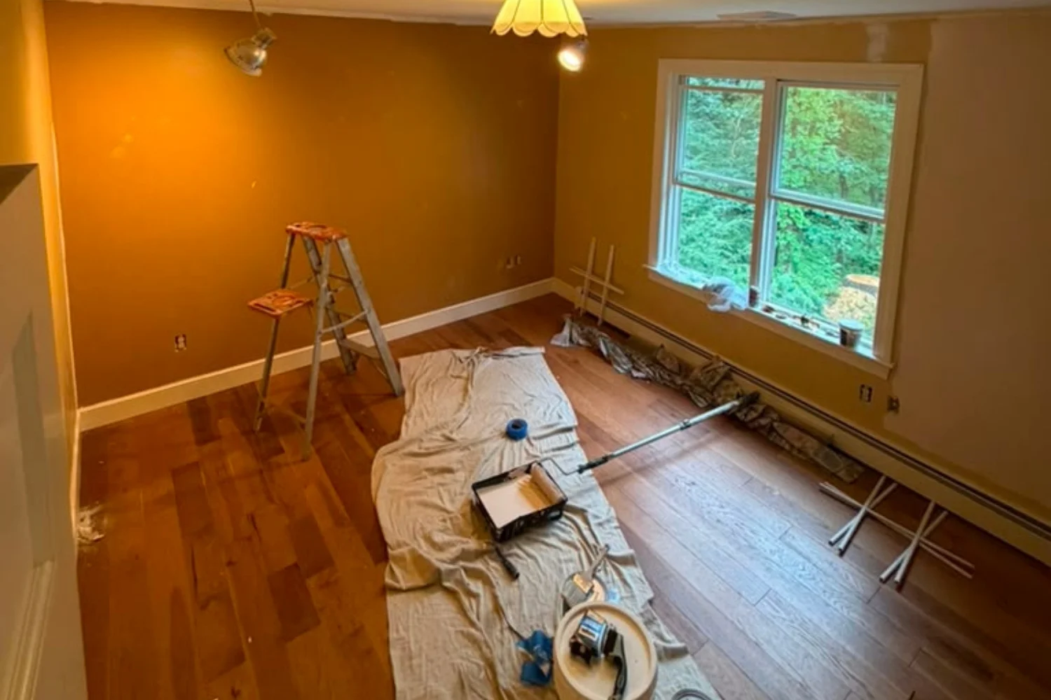 Room being painted in a warm ochre tone with ladder, roller and drop cloth
