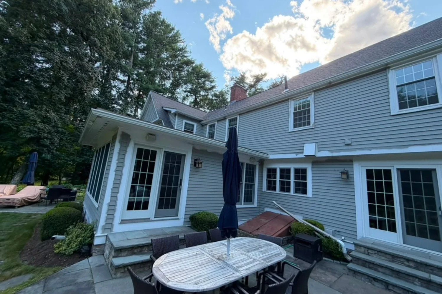 Rear exterior of a home with blue-gray siding and stone patio
