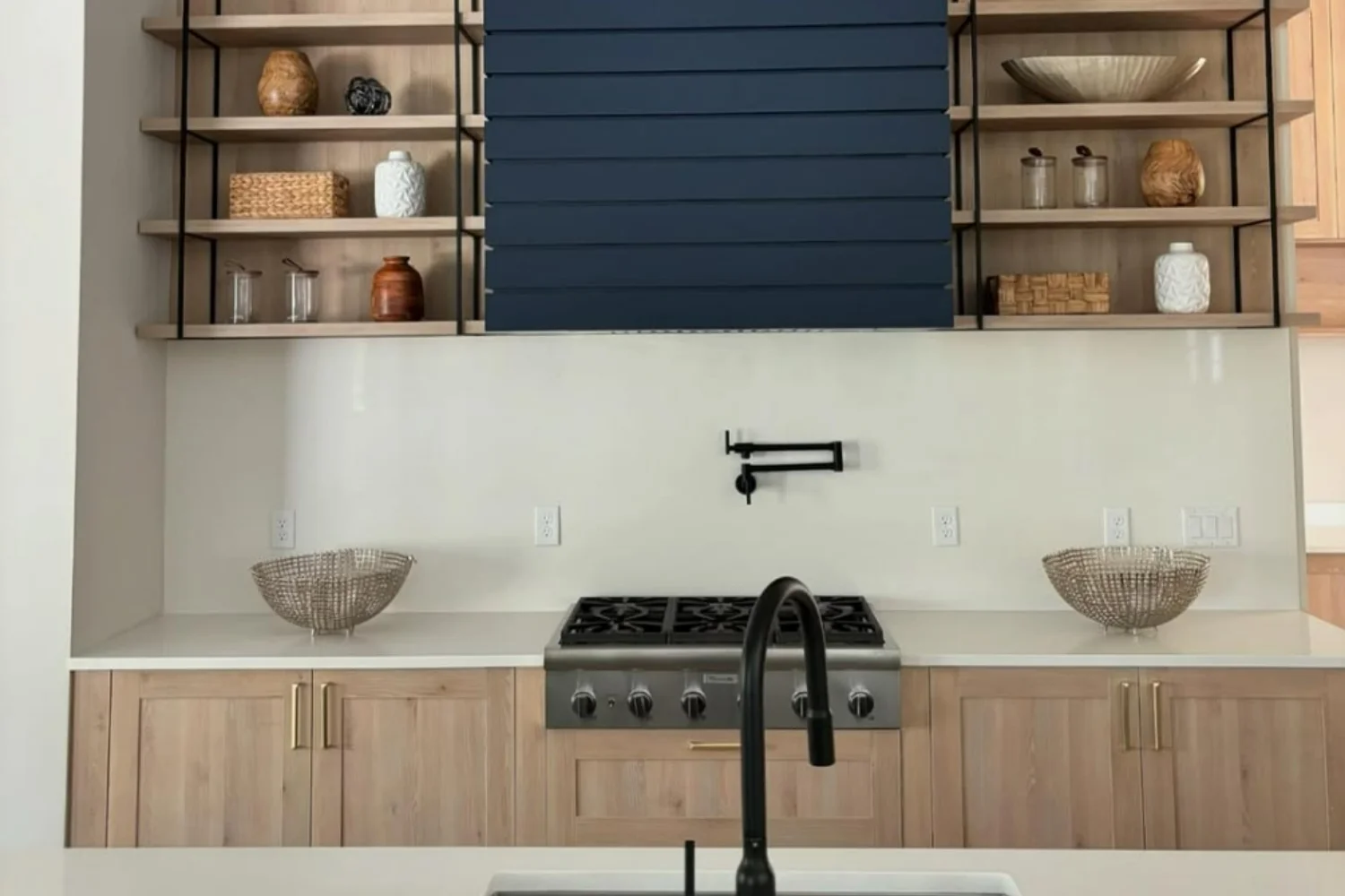 Finished kitchen with navy blue slatted range hood, open shelving and light wood cabinets